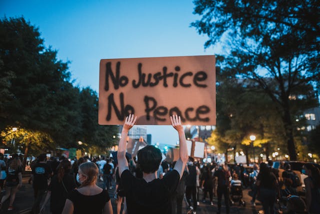 Image of a protest with a man holding a sign that says No Justice No Peace.