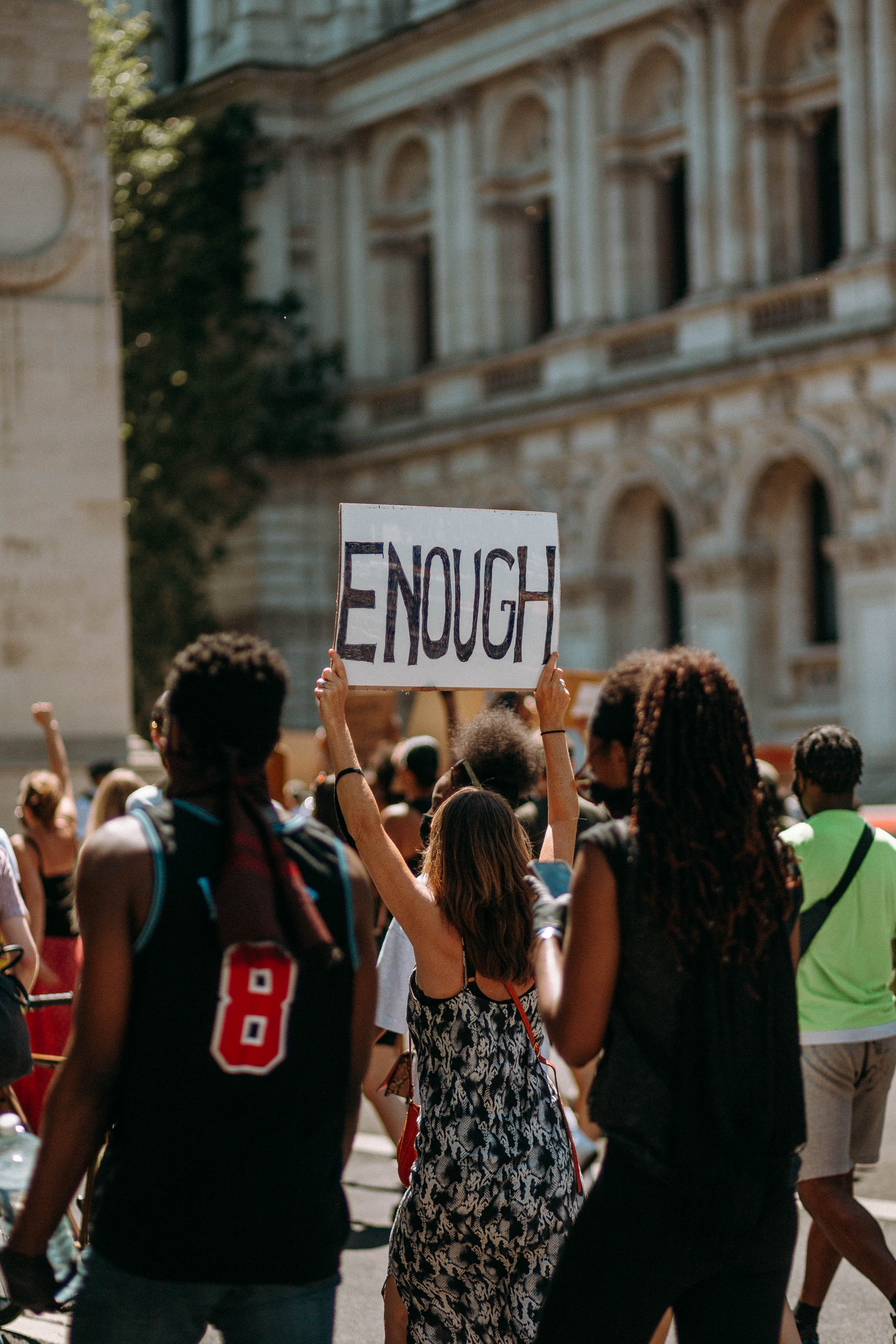 Image of a protest with a woman holding a sign that says Enough.